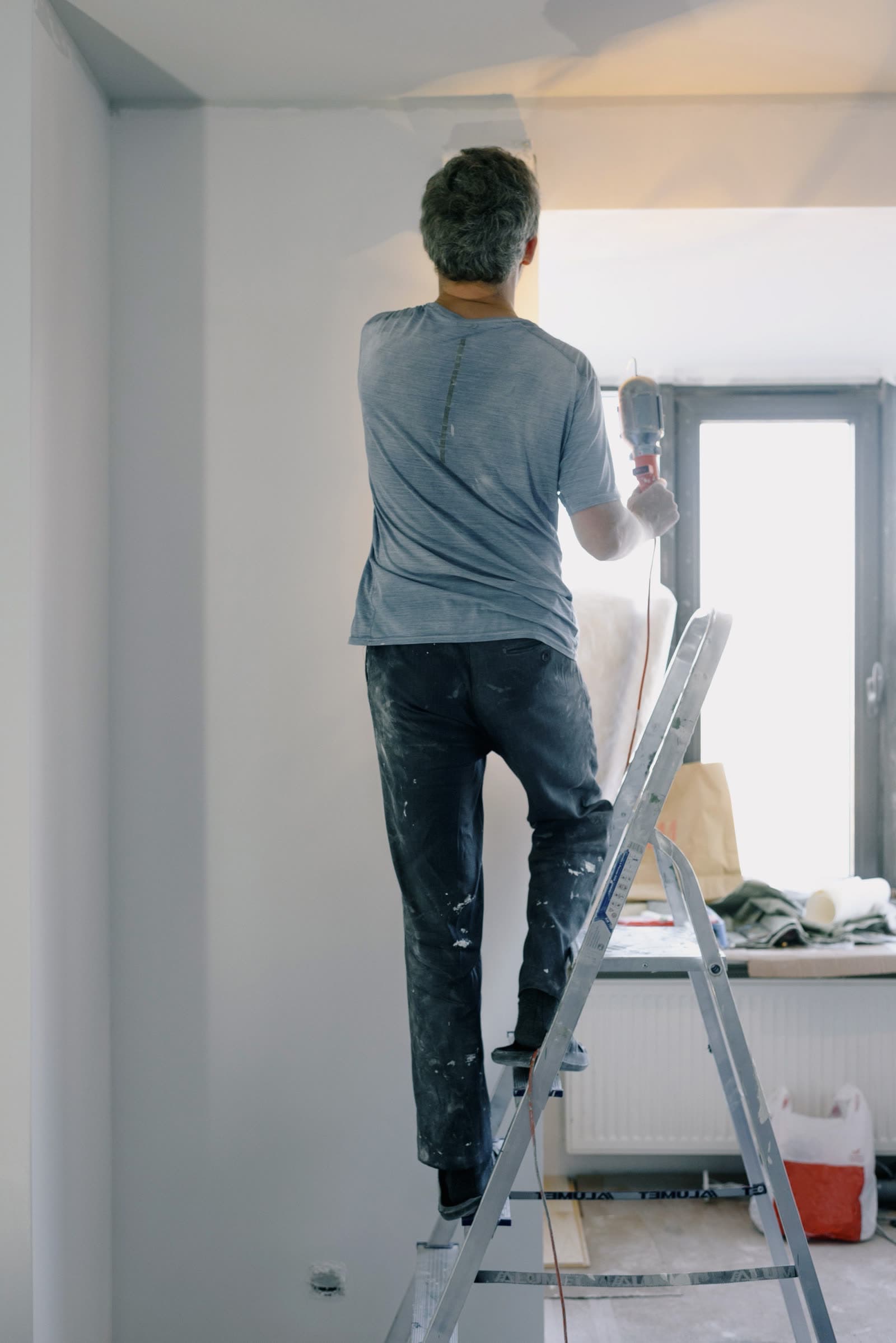 A builder on a stepladder working on an apartment wall