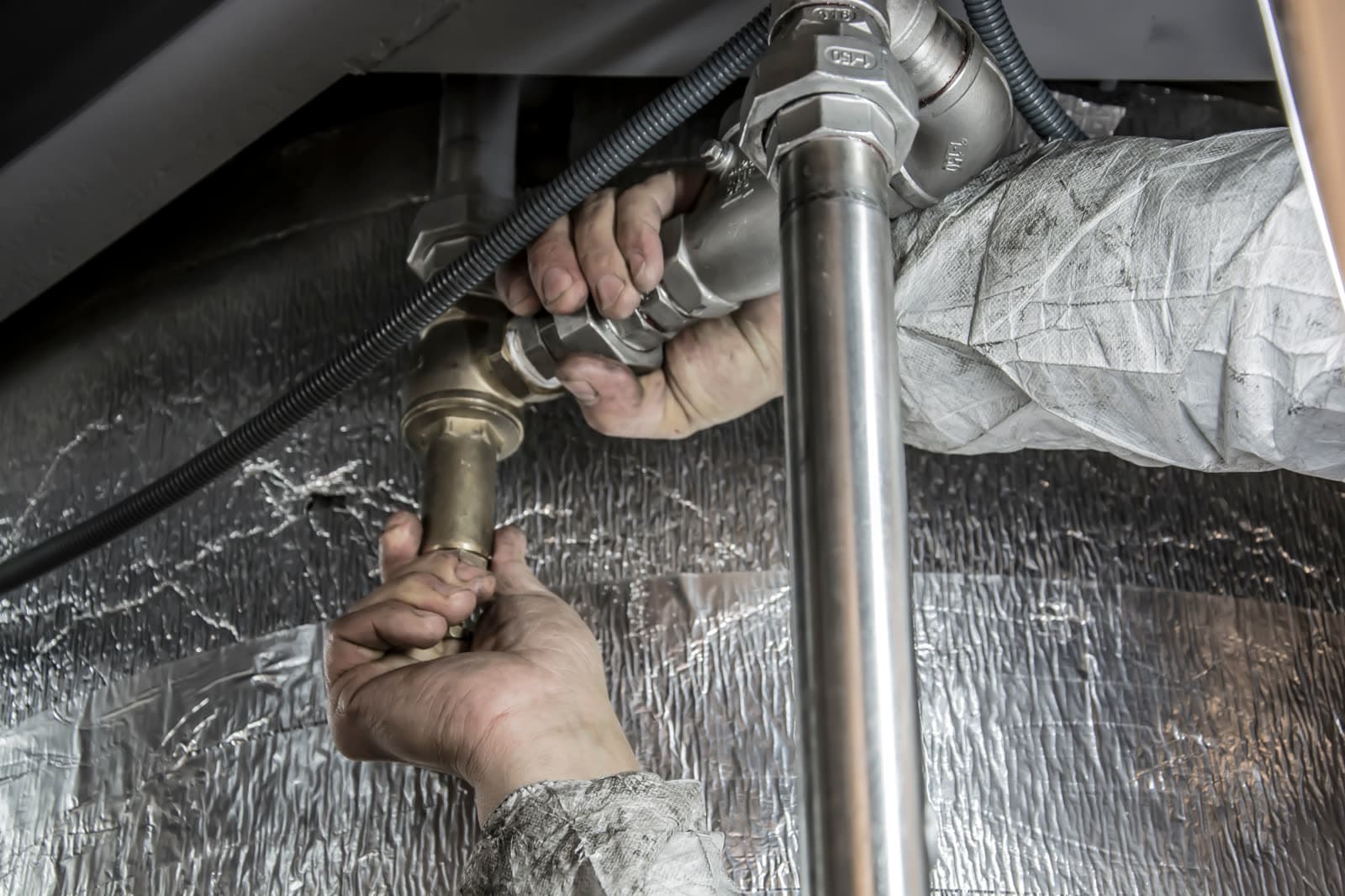 Hands tightening a brass fitting on a water pipe